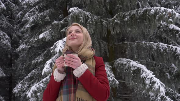 Beautiful blonde woman with cup of coffee in snow forest