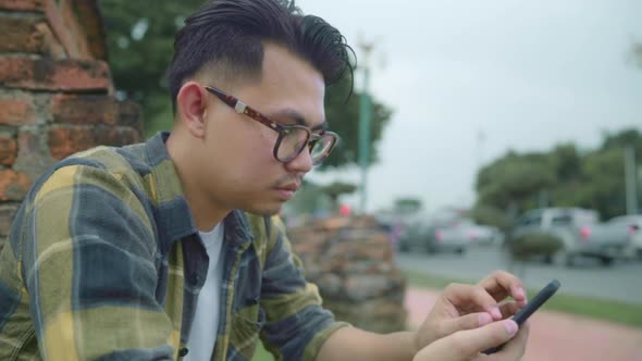 Asian man using smartphone check social media while relax after spending holiday trip at Ayutthaya