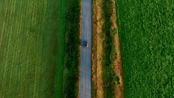 Top View of a Car Driving on the Road in a Field at Sunset in Summer