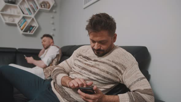 Gay Couple Sitting on the Oposite Sides of the Couch and Looking at Their Phones