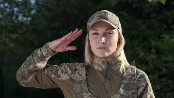 Female Soldier in Camouflage Uniform is Saluting and Looking at Camera