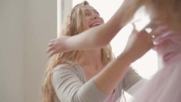 Beautiful Caucasian Mother with Long Blond Hair and Little Daughter Hugging at Home