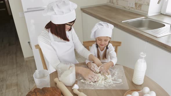 Cute Girl and Her Beautiful Mom in Hats of Chef and Apron for Cooking are Looking at Each Other