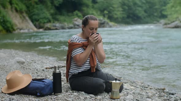 Smiling  Woman drinks mocha coffee and looking at mountain river, road trip and staycation concept