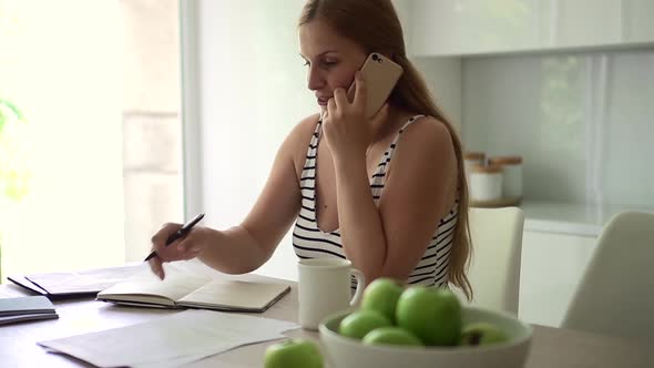 Woman Talking on Phone and Working at Table in Home Kitchen Indoors Spbd