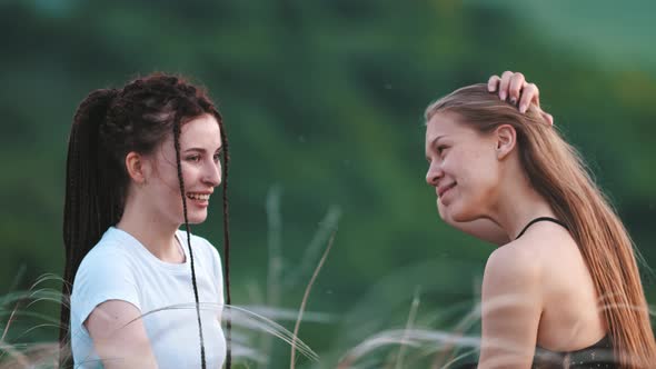 Two Young Happy Women Sitting in Grass and Talking