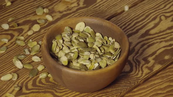 SLOW: Peeled Pumpkin Seeds Fall Into A Wooden Dish On A Table