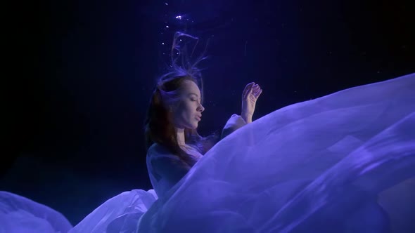 a Beautiful Brunette with Long Hair Slowly Descends Into a Cloud of White Cloth in the Darkness