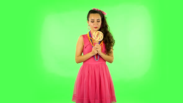 Girl with Great Pleasure Eats a Large Multi-colored Candy While Enjoying. Green Screen