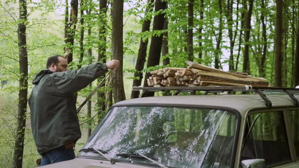 Slow Motion Of Casual Strong Man Works with Firewood and Rope Near Car in Wild Deciduous Forest.