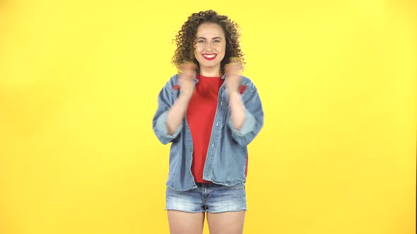 Girl Claps Her Hands with Joy and Delight, Then Shows the Sign Like on Yellow Background at Studio.