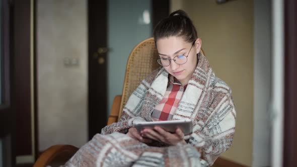 Girl in chair with a tablet in her hands surfing the Internet or reading a book