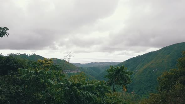 Drone flying up over some trees to reveal a huge forest covered valley surrounded by mountains in ce