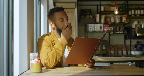 Front view of young mixed-race man looking at menu in cafe 4k