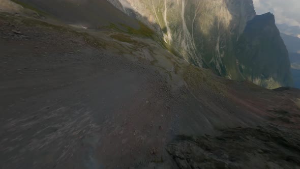 FPV Drone Drop Diving From Summit Mountain Into Valley Cliff Surface Cracked Texture Green Grass