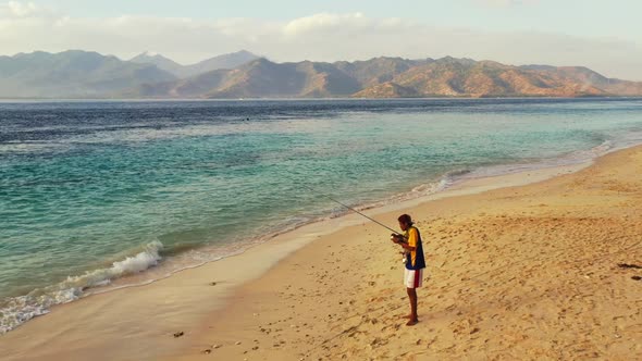 Single guy fishing on paradise lagoon beach adventure by aqua blue sea and white sandy background of