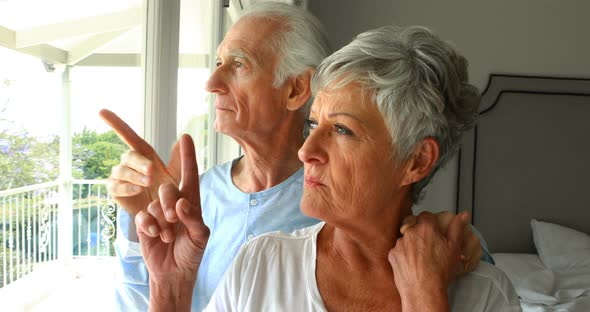 Senior couple looking through window in bedroom