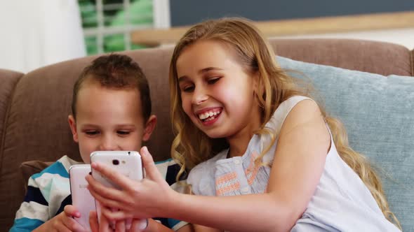 Smiling boy and girl sitting on sofa and using mobile phone