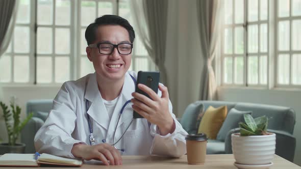 Asian Man Doctor Video Call On Mobile Phone At Home Office