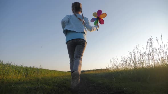 Cheerful Girl Are Running in the Meadow with Wind Turbines As a Sign of Freedom. Happy Child Holding