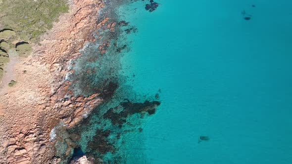 Aerial drone topdown moving towards the ocean with crystal clear calm turquoise water in castle rock