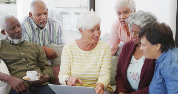 Happy senior diverse people talking and using laptop at retirement home