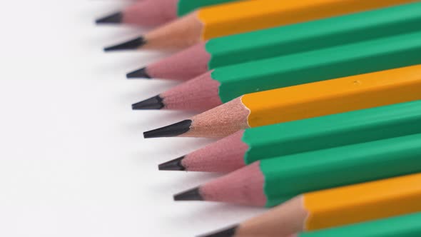 Sharpened graphite green and yellow simple pencils on a white background close-up. Rotation