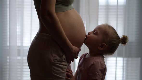 Little girl kissing her young mom's pregnant belly