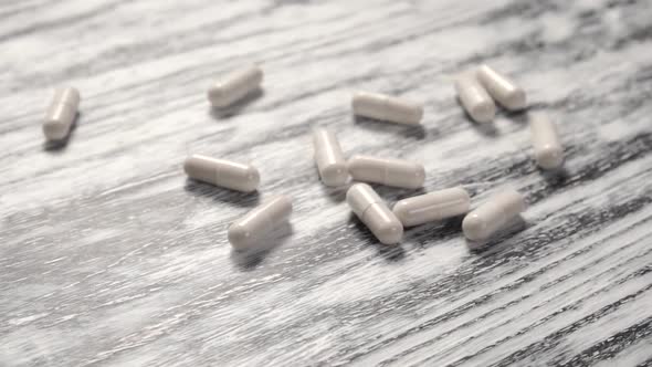 White medical capsules fall into a pile on a wooden old textural black and white table.