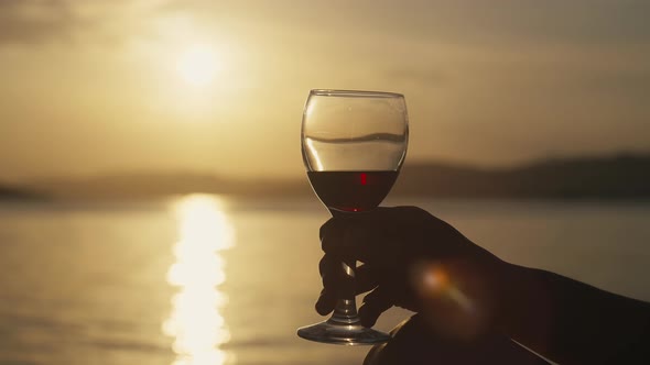 Female Hands Holding a Glass at Sunset in the Seascape