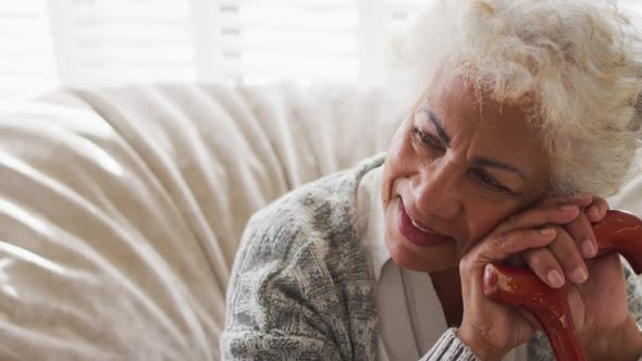 African american senior woman holding walking stick smiling while sitting on a bean bag at home