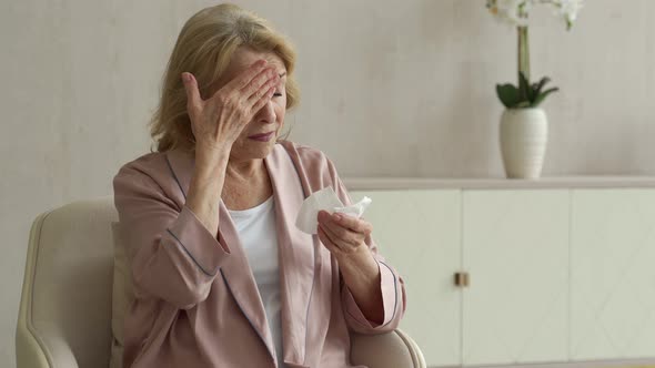 A Sick Elderly Woman Sneezes Using a Paper Napkin for Her Nose She Has a Runny Nose and Coughs