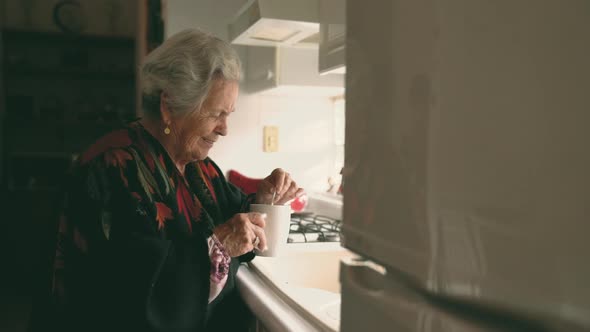 Smiling senior woman in warm clothes with mug near sink
