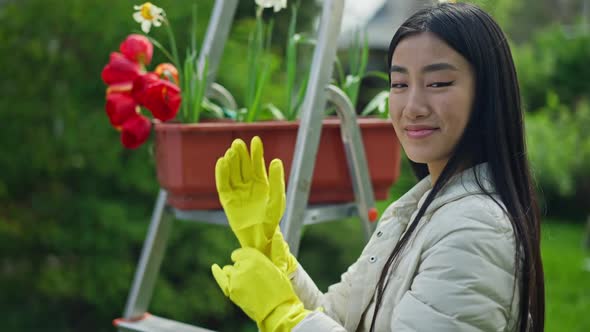 Slim Confident Asian Female Gardener Putting on Yellow Gloves Smiling Looking at Camera