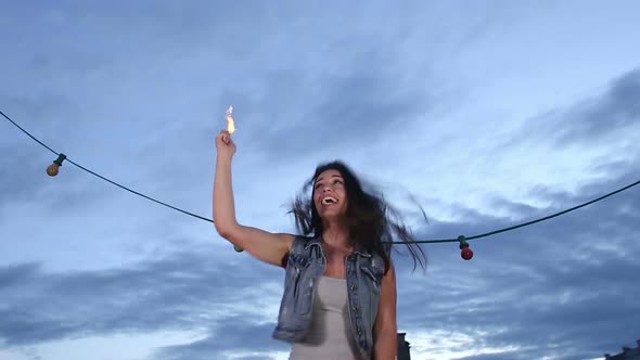 Beautiful woman jumping and waving with firework candle on the rooftop terrace