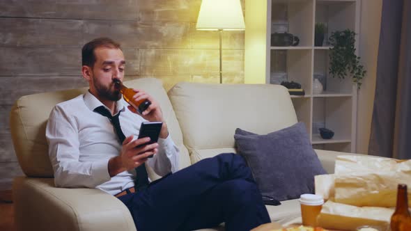 Tired Businessman Sitting on Couch Scrolling on His Phone