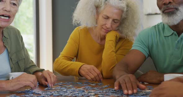 Happy senior diverse people playing puzzle at table at retirement home