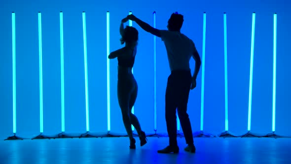 Dancers Practice a Series of Spins Against a Backdrop of Bright Blue Neon Lights in a Dark Studio