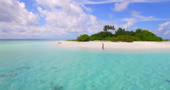 Aerial view of a man walking on the beach around a tiny deserted tropical island.