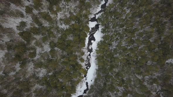 Drone flying high above snowy mountain river in winter