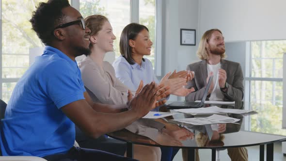 Coworkers Applauding Celebrating Business Success Sitting at Desk During Corporate Meeting in Office