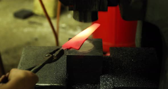 Bladesmith working with hot blade at hydraulic press