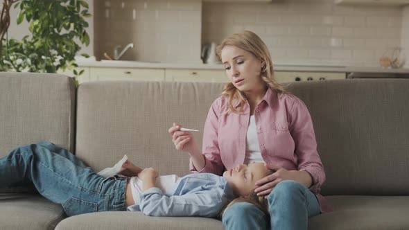 Mother Checking Her Daughter's Body Temperature Sad Little Girl Laying on Sofa