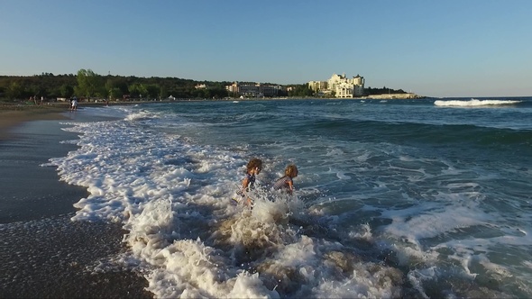 Two girls play and tumble rolling in the beating sea waves