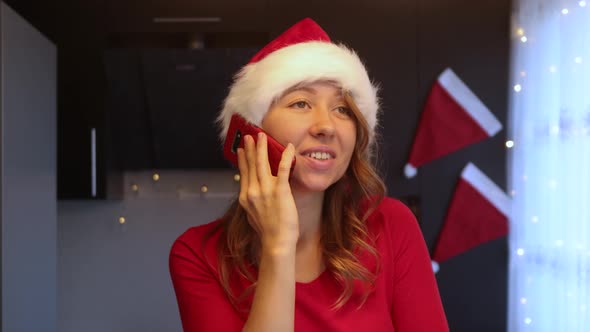 Girl in a red christmas suit in the kitchen talking emotionally on a smartphone