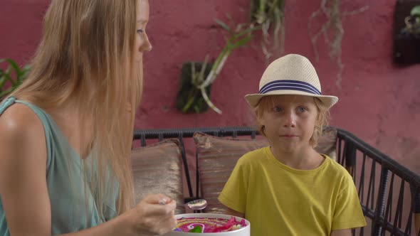 Young Woman and Her Little Son Enjoy Colorful Granola Smoothie in the Bowl Sitting in a Beautiful