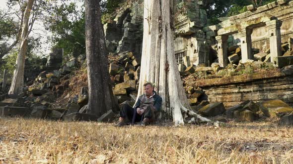 Cambodian Temple Ruins and an Explorer Sitting By the Old Tree