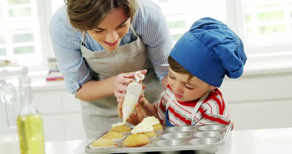 Mother helping boy to decorate cupcake with cream