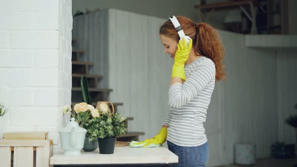 Happy Young Housewife in Rubber Gloves Is Listening To Music Through Headphones and Singing During