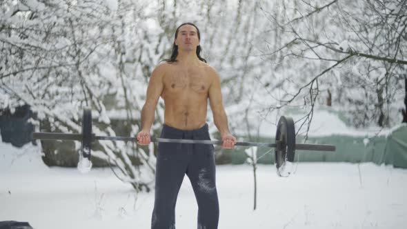 the Guy is an Athlete with Long Black Hair and a Naked Torso Trains in Weightlifting